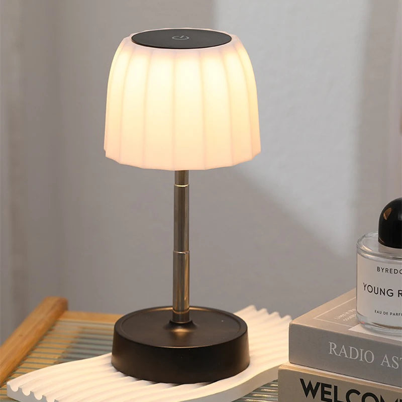 Warm LED desk lamp with black base and gold stem, glowing white pleated shade