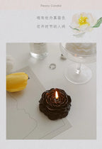 Dark peony sculptural candle with lit wick on a flat card, surrounded by other candles