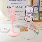 Blush pink rabbit phone stand with circular mesh face, upright ears, and raised phone platform