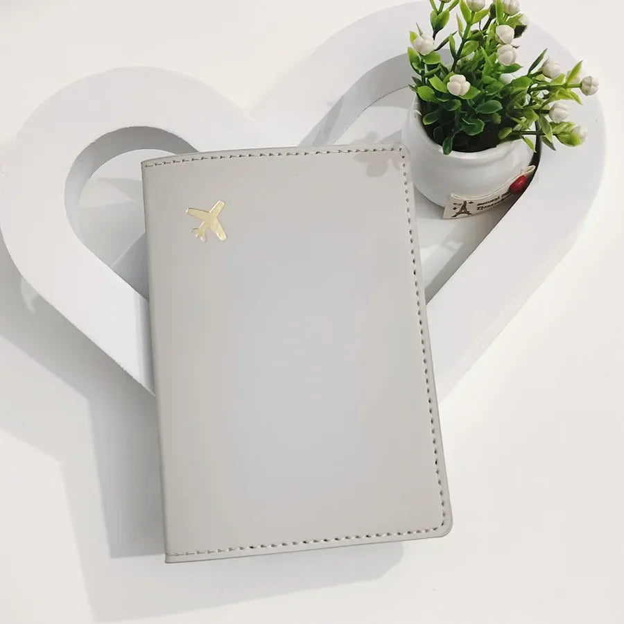 Ivory white passport sleeve with gold airplane emblem and stitched edges