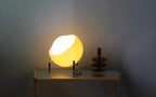 Small amber glow globe table lamp with chrome ring legs on wooden surface