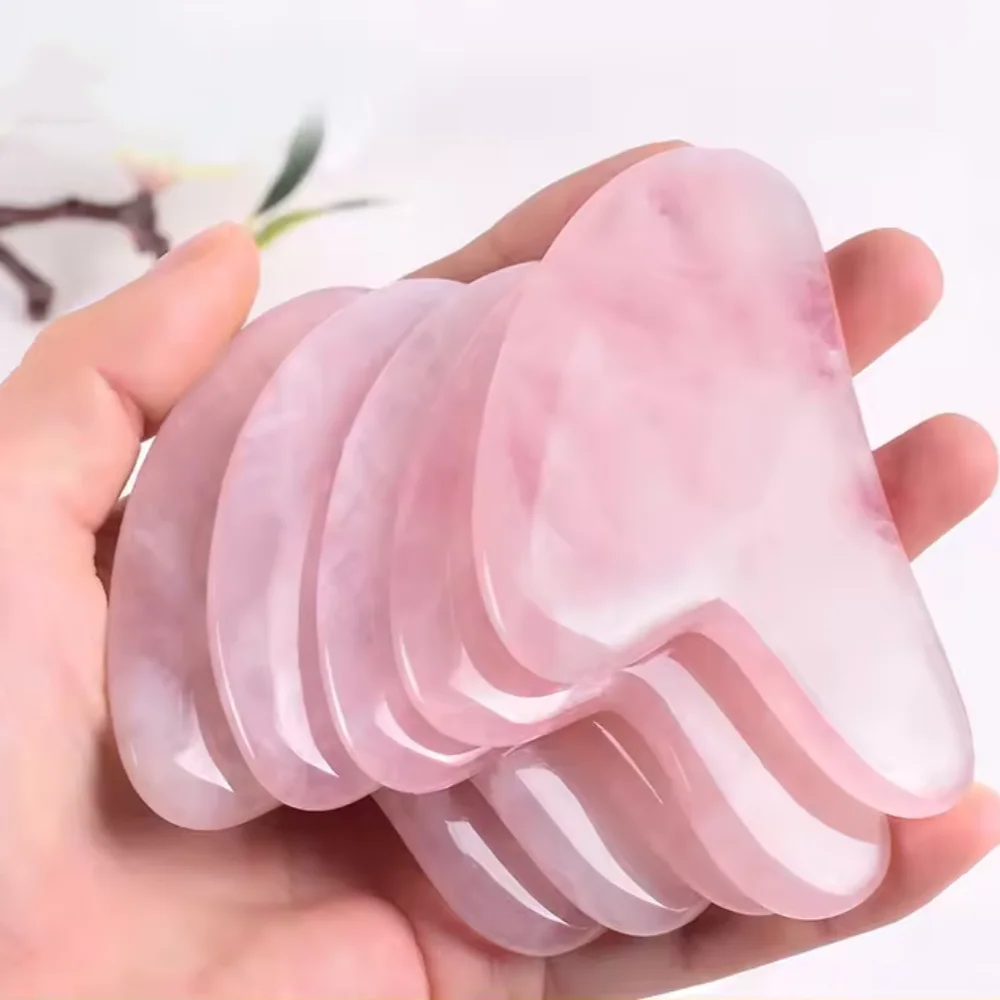 Rose quartz gua sha stone held in hand, smooth polished surface