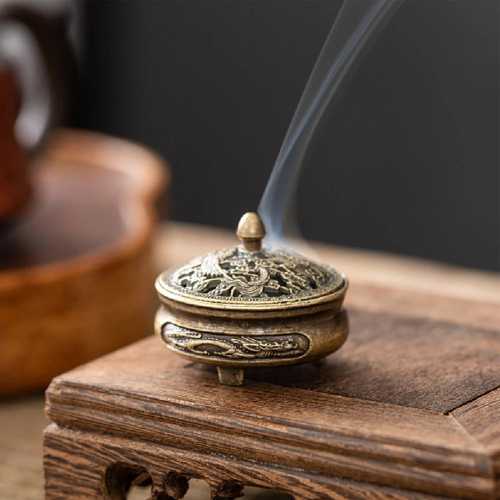 Brass pocket incense burner on wooden tray with dragon-engraved lid and incense stick