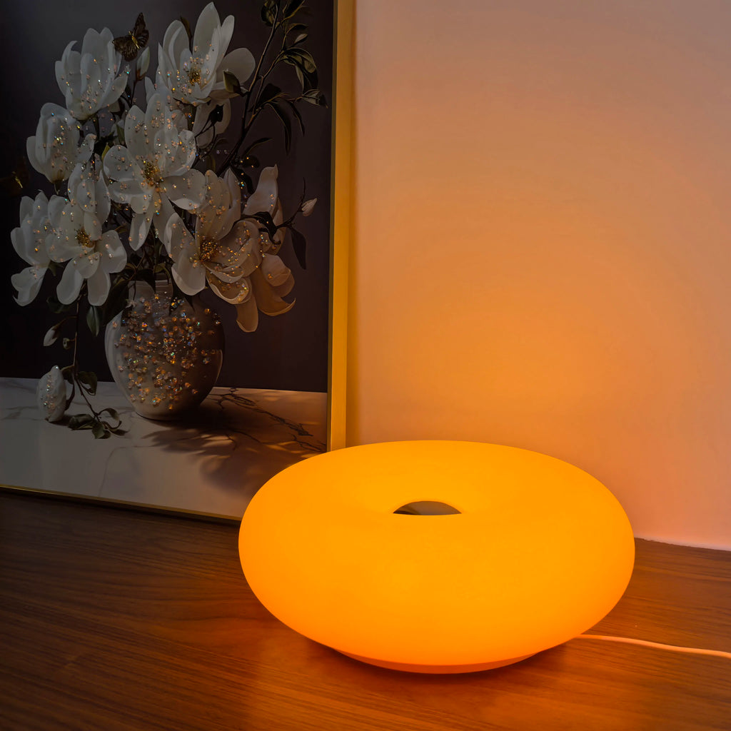 Amber orange donut table lamp with center cutout, glowing on a wooden surface