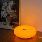 Amber orange donut table lamp with center cutout, glowing on a wooden surface