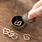 Brass incense burner insert with lid lifted, showing curved opening and engraved motif