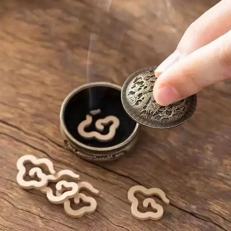 Brass incense burner insert with lid lifted, showing curved opening and engraved motif