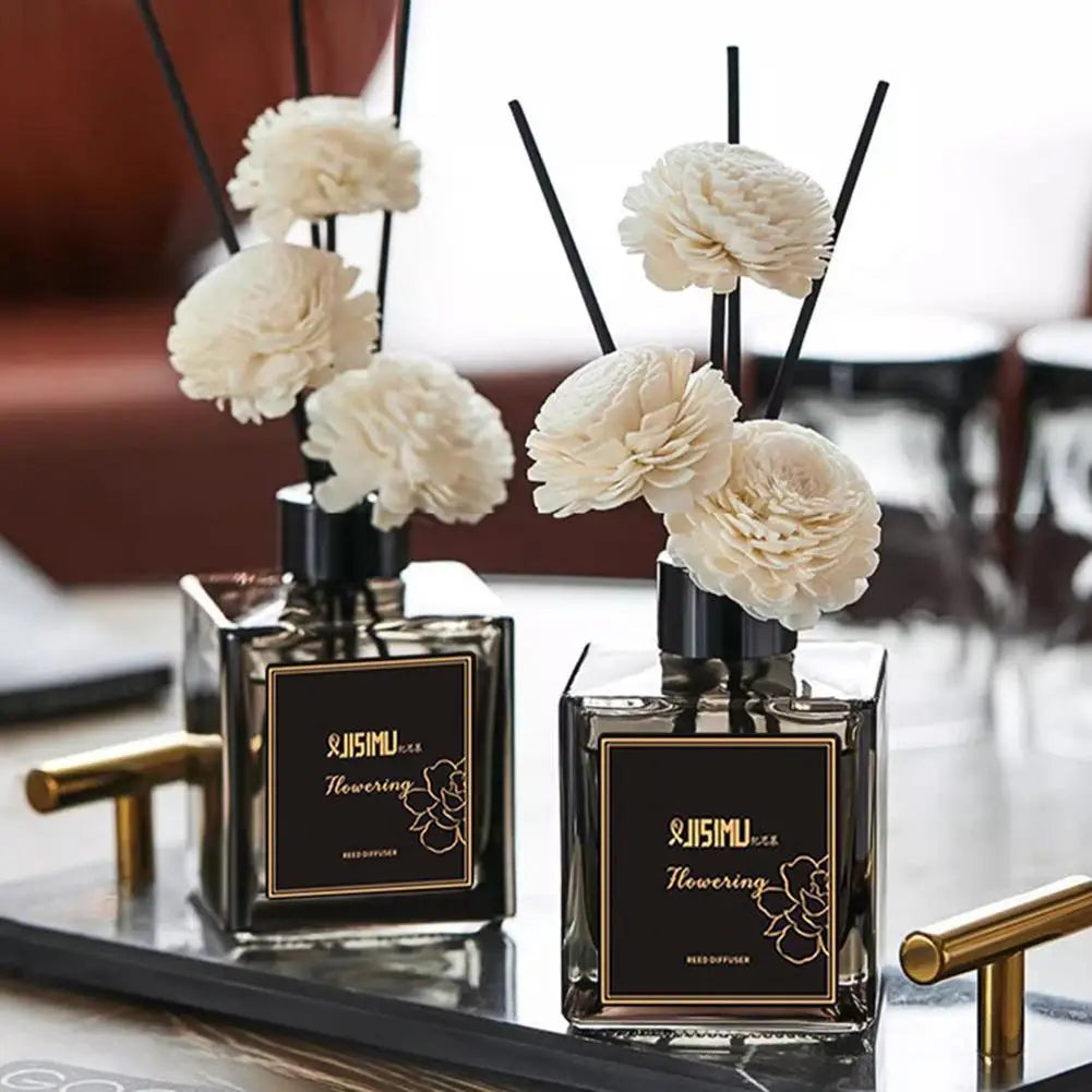 Two mini reed diffusers on tray: square bottles with black reeds and white pom‑pom flowers