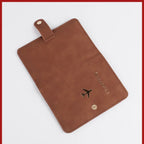 Cognac brown passport folio with airplane emblem, top handle tab, stitched corners