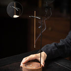 Inverted incense holder on wooden base with black metal stand, incense rising