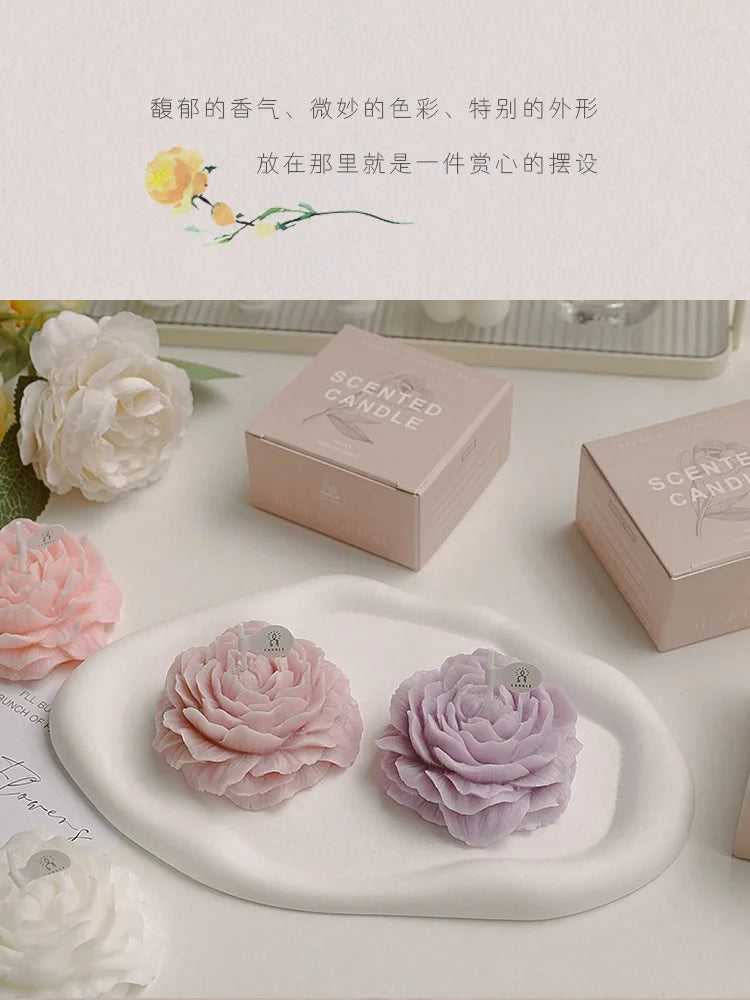 Two peony sculptural candles on a tray: light pink and lavender, with gift boxes nearby