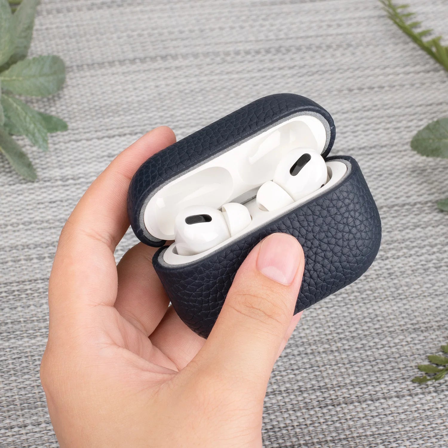 Dark blue leather AirPods Pro case held in hand, earbuds visible with lid open