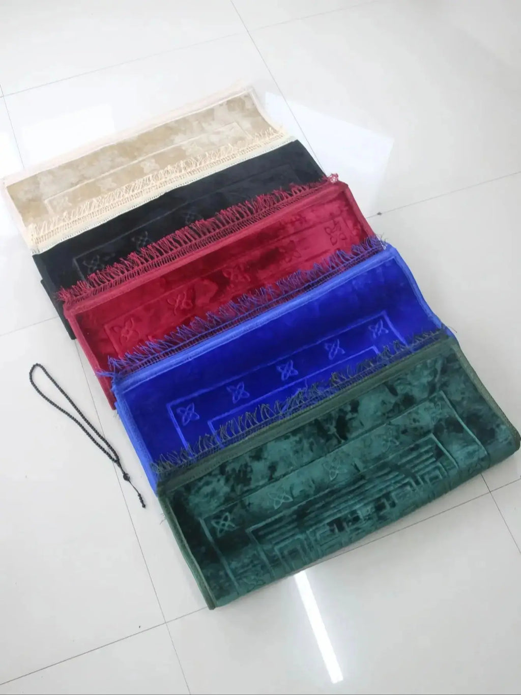 Velvet padded prayer rug in stacked colors: beige top, black, red, blue, green with fringes.