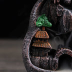 Resin waterfall incense burner detail: arched rocks, orange-roof building, green tree beside smoke