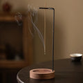 Walnut-black inverted incense holder with smoke above round wooden base
