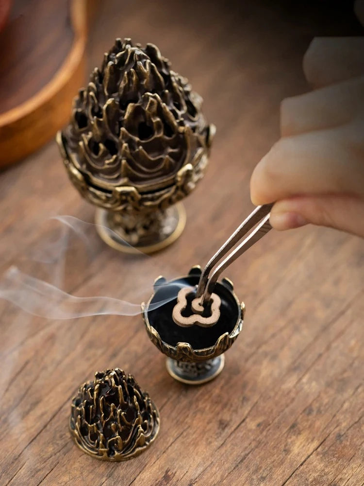 Copper-toned incense censer with flame-lotus top and separate burner cup; smoke from incense.