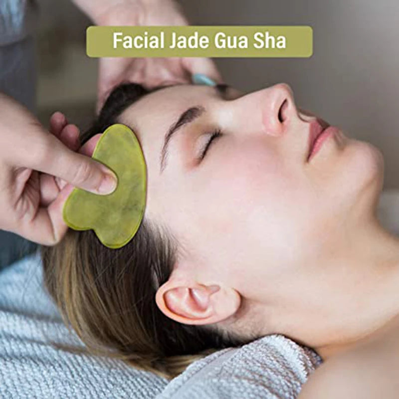 Green jade gua sha heart used on face, held by hand