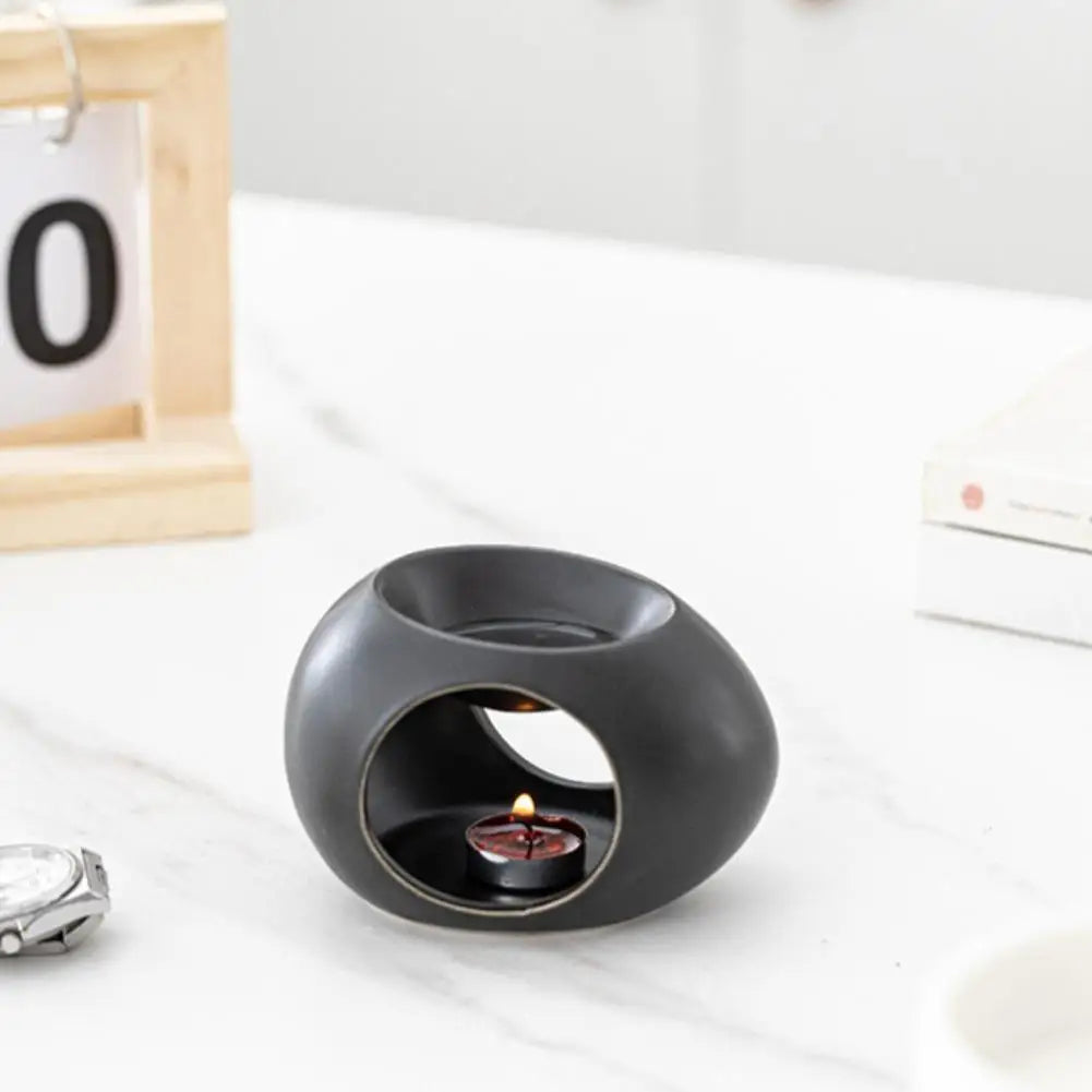 Black ceramic aroma oil burner with open window and lit tea candle on countertop