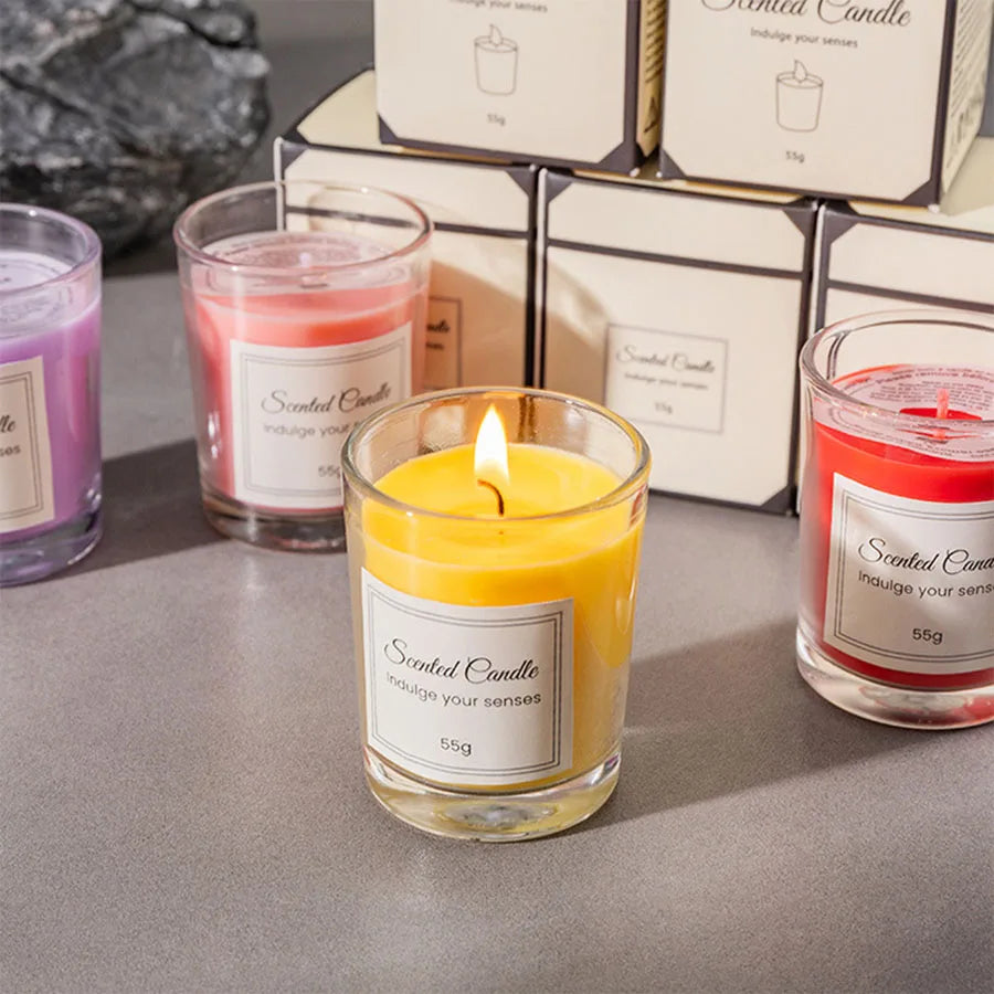 Yellow glass scented candle with lit wick, with surrounding gift boxes