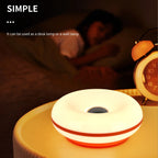 Glowing white donut table lamp on tabletop, warm light from center opening.