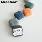 Dark gray Alcantara AirPods case with white AirPods inside; rounded suede texture