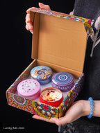 4-piece scented candle gift set in open box with three patterned tins and one lit