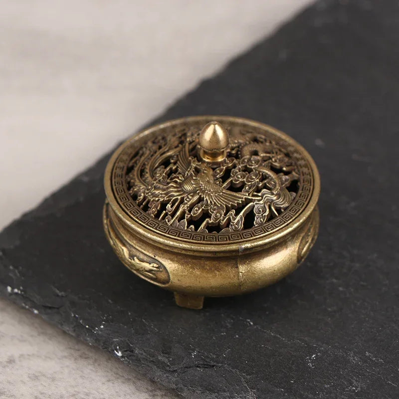 Close-up brass incense plate burner lid on dark stone, detailed dragon relief and spikes