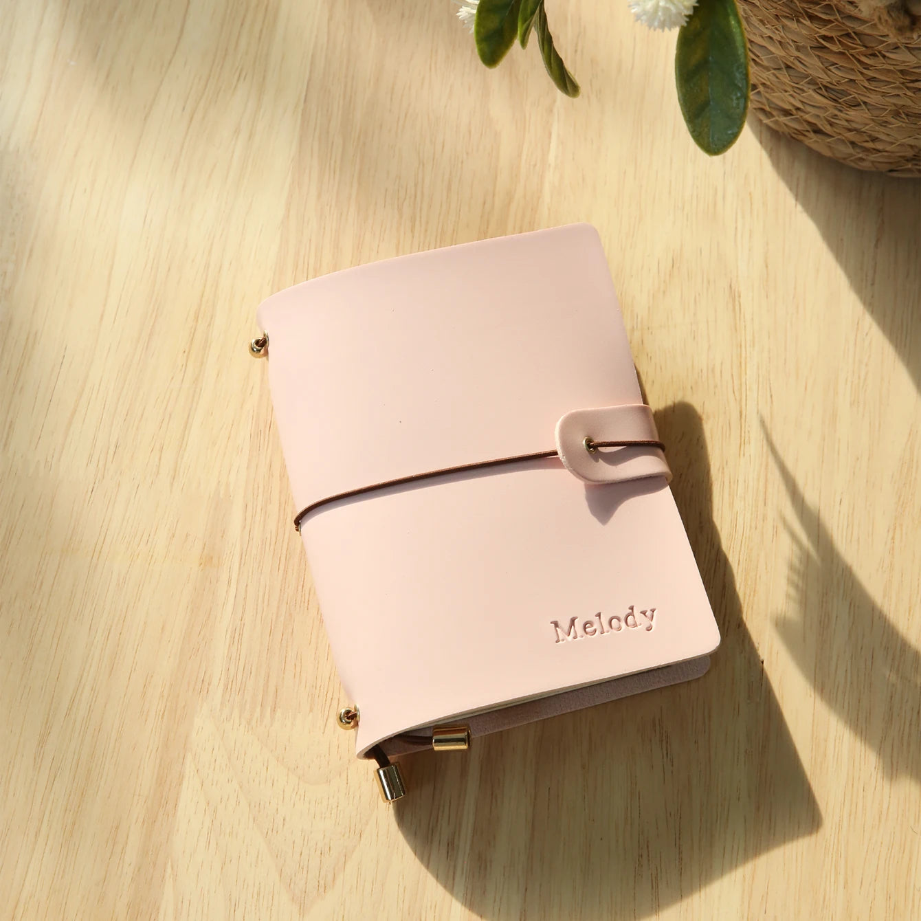 Blush pink passport holder with wrap strap and metal corner clasp, engraved name Melody