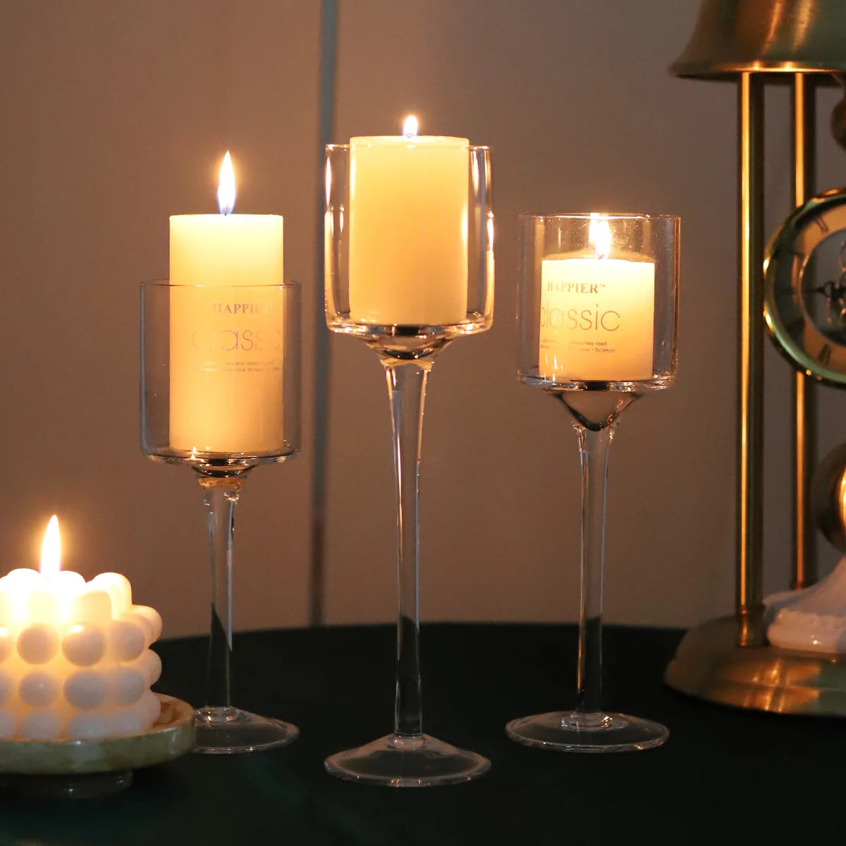 Three lit glass candle holders with clear cups and flat round bases