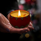 Red patterned scented candle jar with lit flame