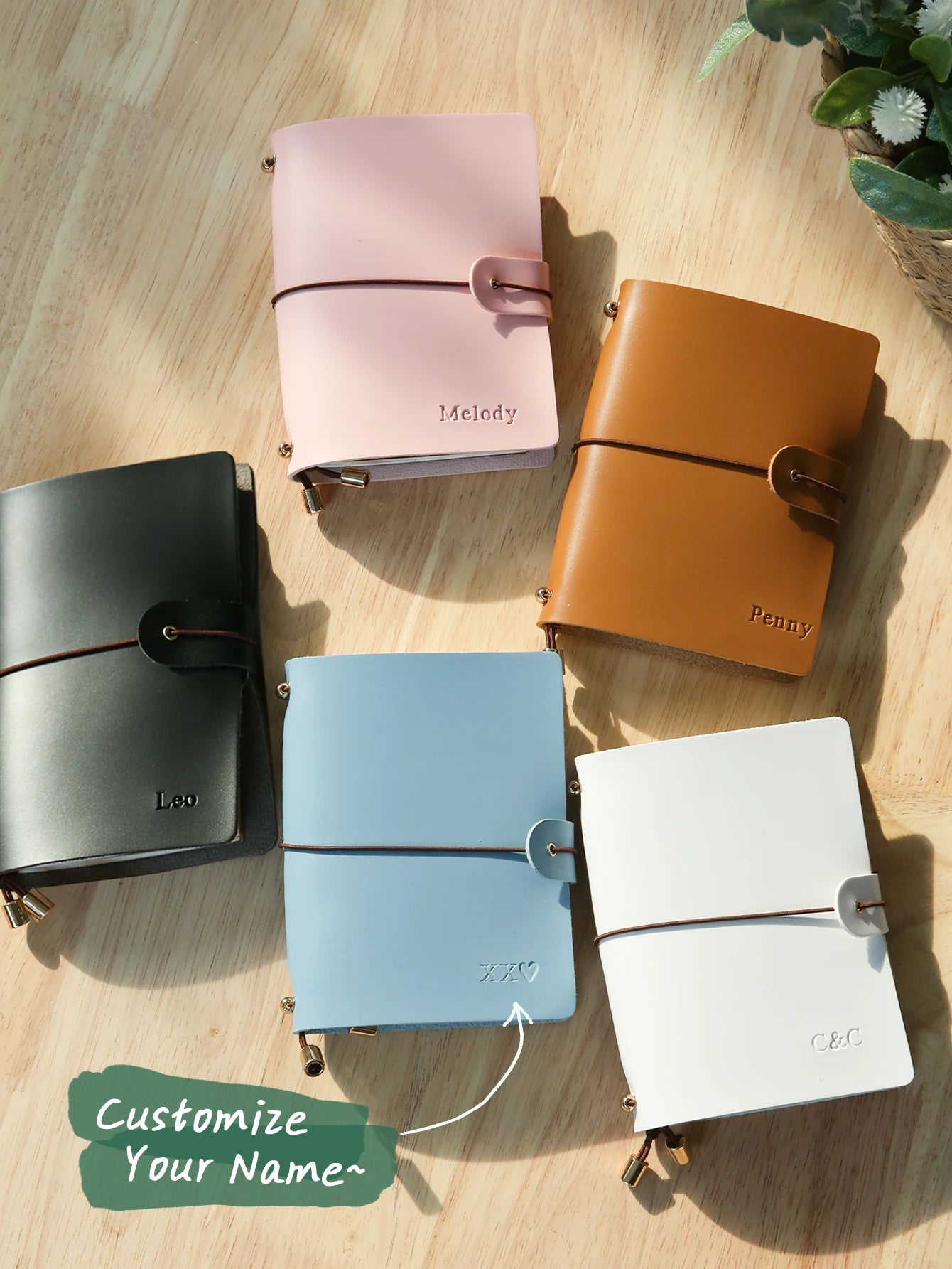 Assorted vegan leather passport holders with buckle straps in black, green, blue, tan, pink, and white