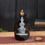 Glazed dark backflow incense bottle burner with cone incense and wisps of smoke