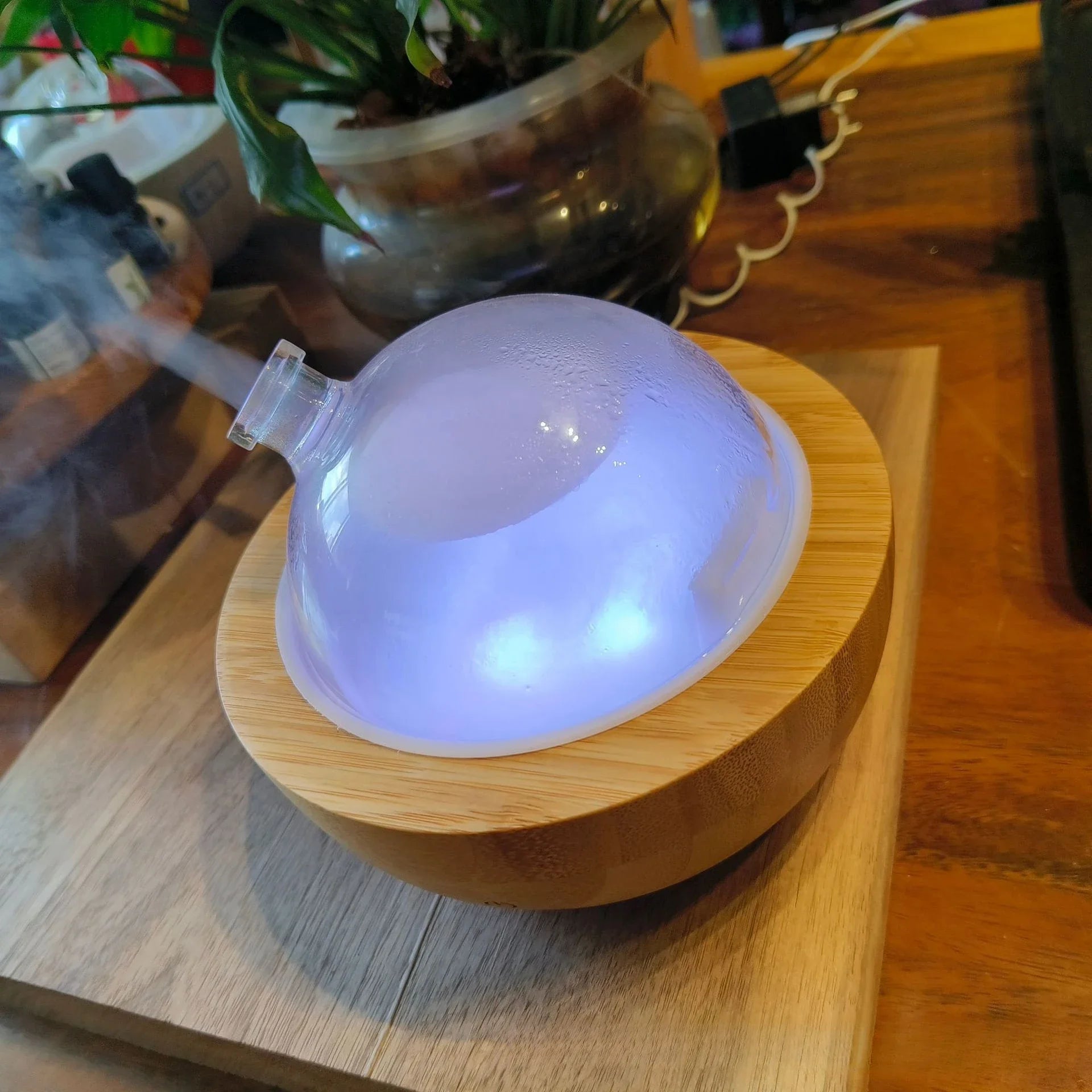 Aroma diffuser dome close view on Natural Wood base, soft blue glow behind the glass