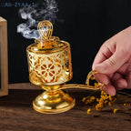 Arabesque incense burner in gold, pierced cylinder with ornate lid; hand holds the handle