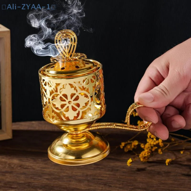 Arabesque incense burner in gold, pierced cylinder with ornate lid; hand holds the handle
