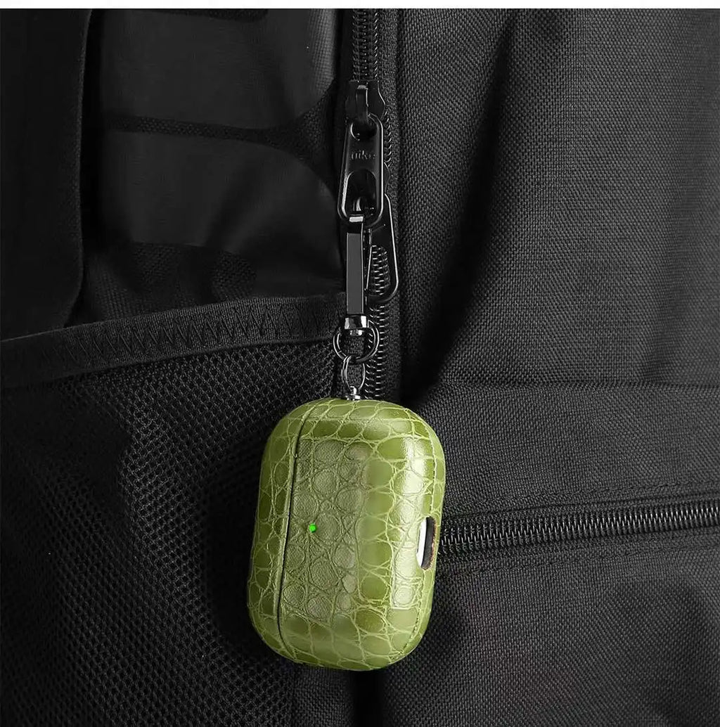 Olive green crocodile-grain AirPods case hanging from zipper pull with clip