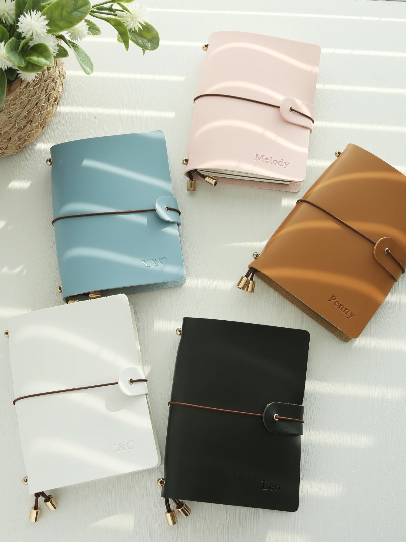 Vegan leather passport holders in light blue, pink, tan, white, and black with buckle straps