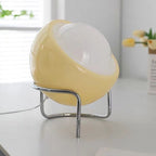 Cream-yellow glass globe table lamp with chrome frame and glowing oval diffuser