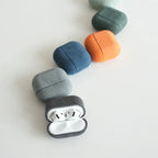 Dark gray Alcantara AirPods case with white AirPods inside; rounded suede texture