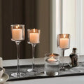 Tall glass candle holder set of 3 with clear stems and round holders, lit candles inside