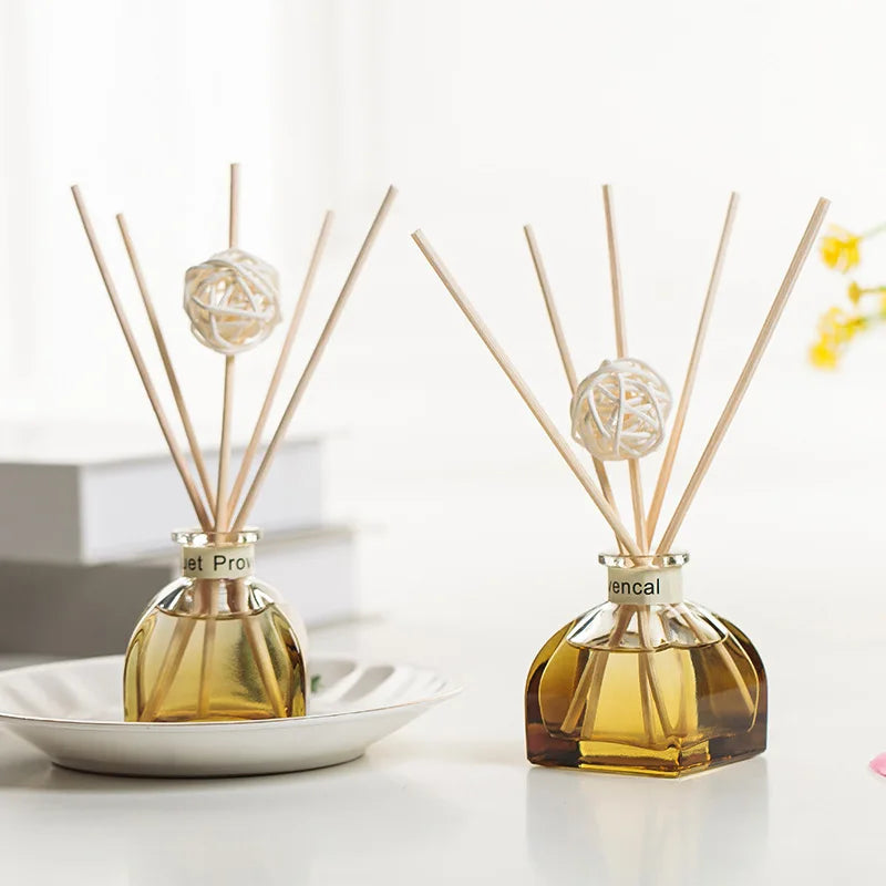 Two floral reed diffuser bottles with amber glass, gold cap, and white woven balls