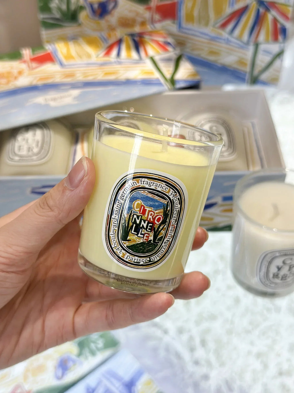 Bougie citronnelle 190 g : pot en verre transparent avec mèche, tenue à la main.