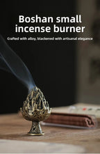 Small boshan incense burner on a tabletop, bronze-gold tiered top with smoke plume.