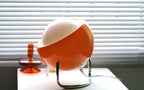 Orange glass globe table lamp with chrome stand and glowing oval diffuser near cord