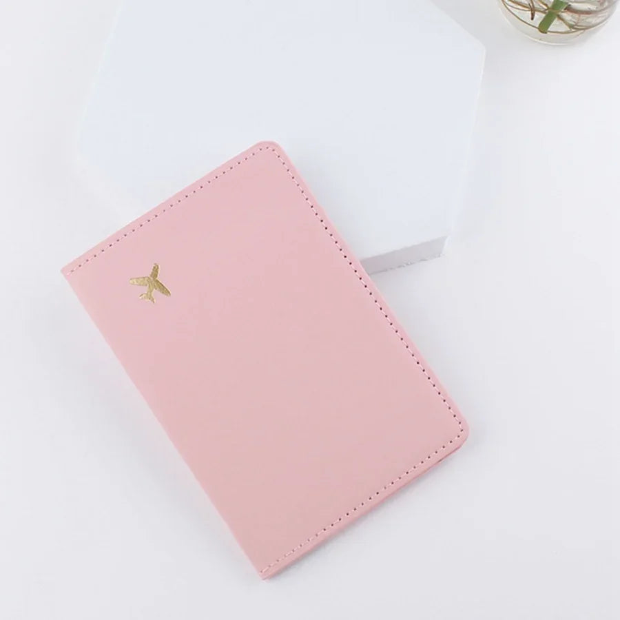 Blush pink passport sleeve with gold plane logo and contrast-stitched edges