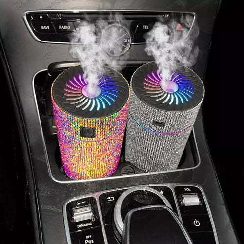 Pair of glitter car aroma diffusers with rainbow and silver bodies, releasing vapor from top vents