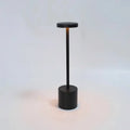Black table lamp with slim vertical stem, round top, and cylindrical base