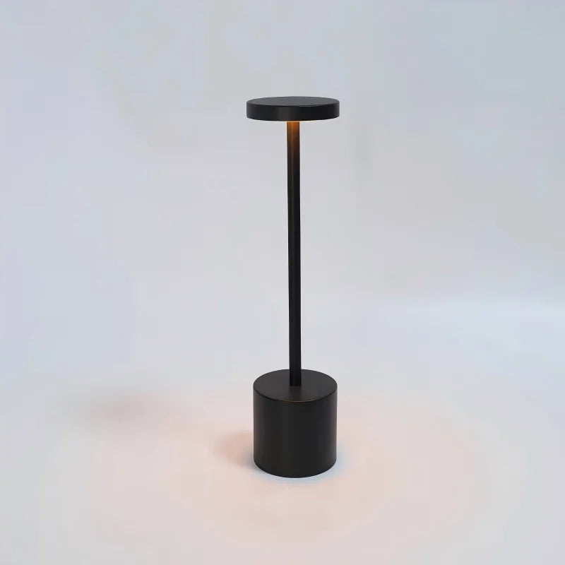 Black table lamp with slim vertical stem, round top, and cylindrical base