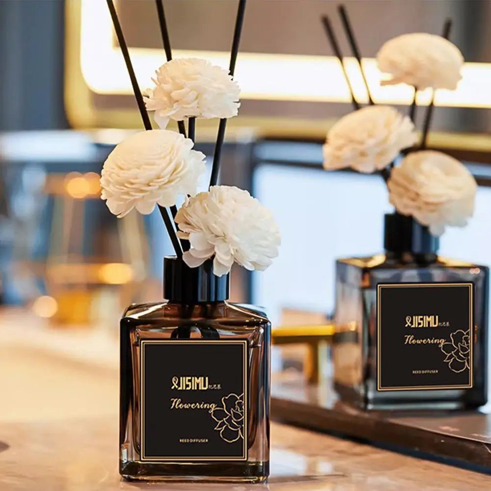 Reed diffuser bottle with black reeds and white pom-pom flowers on a table