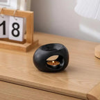 White ceramic aroma oil burner with circular cutout and lit tea candle on ledge